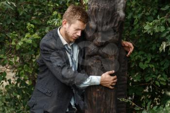 Alone businessman in torn suit hugs wooden statue on desert island. Business risk, collapse or bankruptcy concept