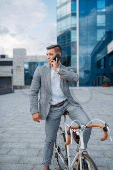 Businessman in suit talking by phone on the bicycle in downtown. Business person riding on eco transport on city street