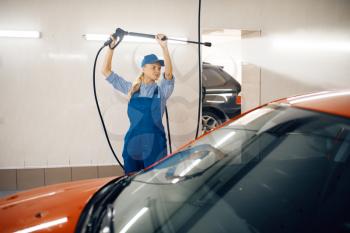 Female washer in uniform cleans the auto with high pressure gun in hands, car wash service. Woman washes vehicle, carwash station, car-wash business