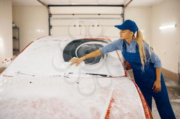 Female washer with sponge wipes the automobile windshield, car wash. Woman cleans vehicle, carwash station, car-wash business