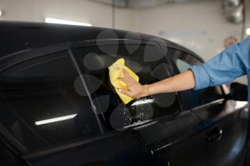 Female washer with sponge wipes the automobile glass, car wash. Woman cleans vehicle, carwash station, car-wash business