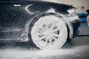 Female washer applies foam to the wheel, car wash. Woman cleans vehicle, carwash station, car wash