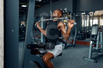 Muscular man in sportswear at exercise machine on training in gym. Workout in sport club, healthy lifestyle