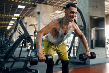 Muscular athlete in sportswear doing exercise with dumbbells on training in gym. Workout in sport club, healthy lifestyle