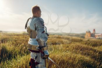 Medieval knight in armor holds sword. Armored ancient warrior in armour posing in the field