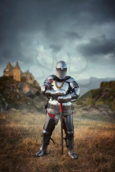 Medieval knight in armor and helmet against castle. Armored ancient warrior in armour in the field