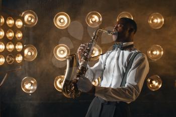 Black jazz performer plays the saxophone on the stage with spotlights. Black jazzman preforming on the scene