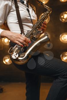 Female saxophonist plays the saxophone on the stage with spotlights. Jazz performer playing on the scene closeup
