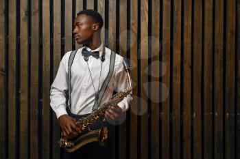 Black jazz performer with saxophone, wooden background. Black jazzman preforming on the scene