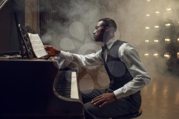 Ebony pianist, jazz performer on the stage with spotlights on background. Negro musician poses at musical instrument before concert