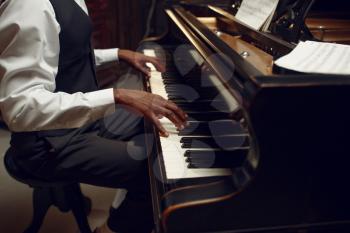 Ebony pianist, jazz performer on the stage with spotlights on background. Negro musician poses at musical instrument before the concert