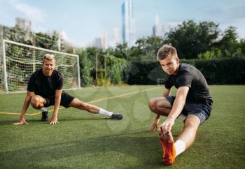 Two male soccer players doing stretching exercise on the field. Football training on outdoor stadium, team workout before game
