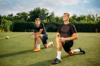 Two male soccer players doing stretching exercise on the field. Football training on outdoor stadium, workout before game