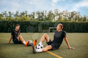 Two male soccer players resting on the grass on the field. Footballers on outdoor stadium, workout before game, football training