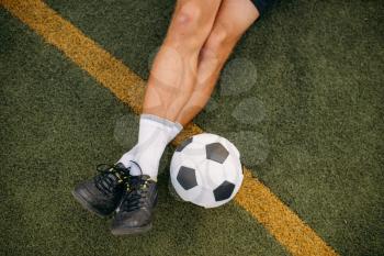 Male soccer player with ball sitting on the grass on the field. Footballer on outdoor stadium, workout before game, football training