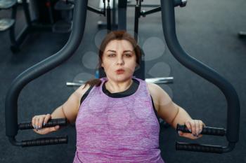 Overweight woman on exercise machine in gym, top view, active training. Female person struggles with excess weight, aerobic workout against obesity, sport club