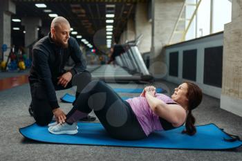 Overweight woman with trainer doing exercise on mat in sport club, fitness training with instructor. Female person struggles with excess weight, aerobic workout against obesity, gym