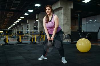 Overweight woman doing exercise with kettlebell in gym, active training. Obese female person struggles with excess weight, aerobic workout against obesity, sport club
