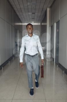 Ebony businessman with briefcase in office hall. Successful business person walking down the corridor, black man in formal wear