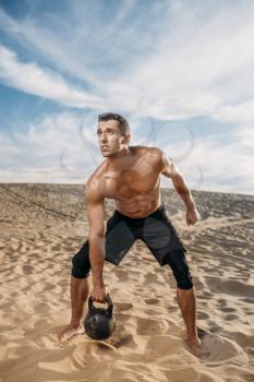Male athlete doing exercises with kettlebell in desert at sunny day. Strong motivation in sport, strength outdoor training
