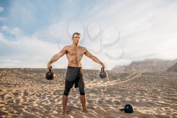 Male athlete doing exercises with two kettlebell in desert at sunny day. Strong motivation in sport, strength outdoor training