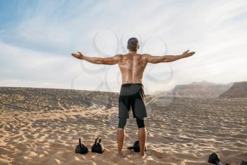 Sportsman doing exercises with weights in desert at sunny day, back view. Strong motivation in sport, strength outdoor training