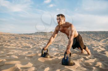 Male athlete doing push-up exercises with two kettlebells in desert at sunny day. Strong motivation in sport, strength outdoor training