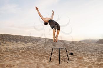 Male athlete makes a jump through himself in desert at sunny day, flying sand effect. Strong motivation in sport, strength outdoor training
