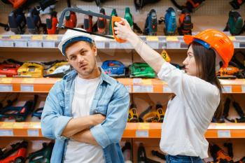 Playful couple choosing tools in hardware store. Male and female customers look at the goods in diy shop