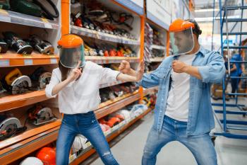 Playful couple fight in hardware store like a children. Male and female customers look at the goods in diy shop