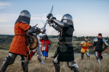 Medieval knights in armour and helmets fight with swords. Armored ancient warriors posing in the meadow