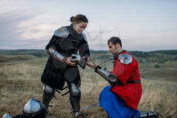 Medieval knight helps his friend to put on armor, great tournament. Armored ancient warrior in armour posing in the field