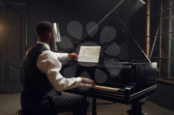 Ebony pianist, jazz performer on the stage with spotlights on background. Negro musician poses at musical instrument before concert