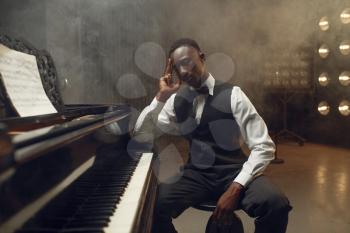 Black grand piano player, jazz performer on the stage with spotlights on background. Black musician poses at musical instrument before concert