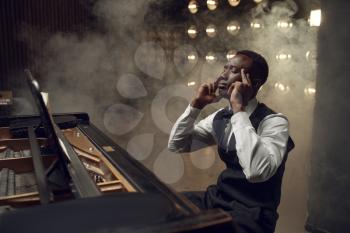Black grand piano musician on the stage with spotlights on background. Black pianist poses at musical instrument before concert