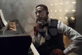 Black grand piano musician poses on the stage with spotlights on background. Black pianist poses at musical instrument before concert