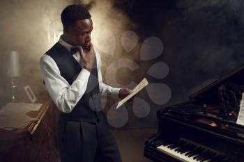 Black pianist with music notebook in his hands on the scene with spotlights on background. Black performer poses at musical instrument before concert