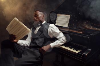 Black pianist with music notebook, jazz musician. Black performer poses at musical instrument before concert