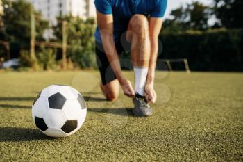 Male soccer player ties his shoelaces on boots, top view. Footballer on outdoor stadium, workout before game, football training