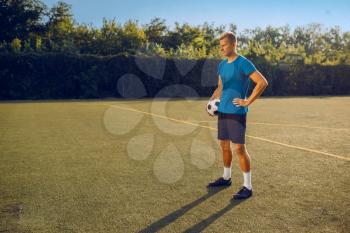 Male soccer player with ball standing on the field. Footballer on outdoor stadium, workout before game, football training