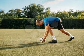Male soccer player prepares to hits the ball on the field. Footballer on outdoor stadium, workout before game, football training