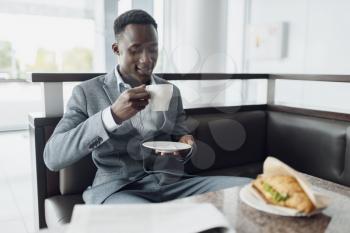 Young black businessman having lunch in office cafe. Successful business person drinks coffee in food-court, black man in formal wear