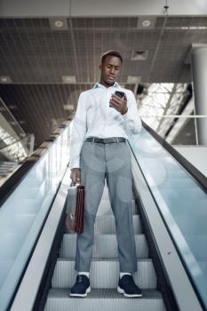 Black businessman with briefcase talking by phone on the escalator in mall. Successful business person, black man in formal wear, shopping center