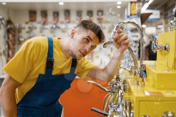 Male builder choosing water tap in hardware store. Constructor in uniform look at the goods in diy shop