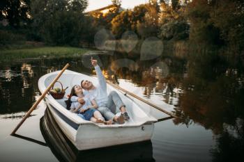 Love couple lying in a boat on quiet lake and dreaming at sunset. Romantic meeting, boating trip, man and woman walking along the river