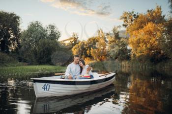 Love couple hugs in a boat on quiet lake at summer day. Romantic meeting, boating trip, man and woman walking along the river