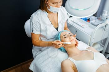 Cosmetician with brush cleans facial skin to female patient, botox preparation. Rejuvenation procedure in beautician salon. Doctor and woman, cosmetic surgery against wrinkles and aging