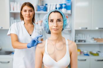 Cosmetician holds botox syringe and female patient with markers on her face. Rejuvenation procedure in beautician salon. Cosmetic surgery against wrinkles and aging