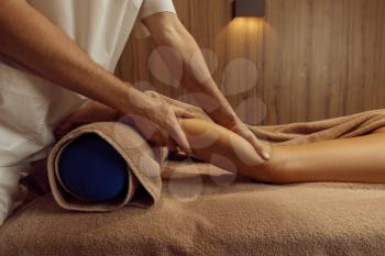 Male masseur stretching legs to young woman in towel, professional massage. Massaging and relaxation therapy, body and skin care. Attractive lady in spa salon