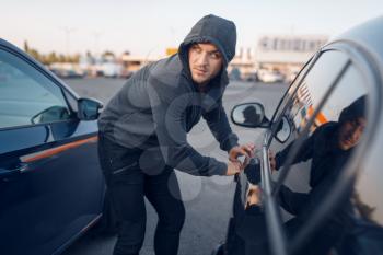 Car thief breaking door lock, criminal lifestyle. Hooded male robber opening vehicle on parking. Auto robbery, automobile crime